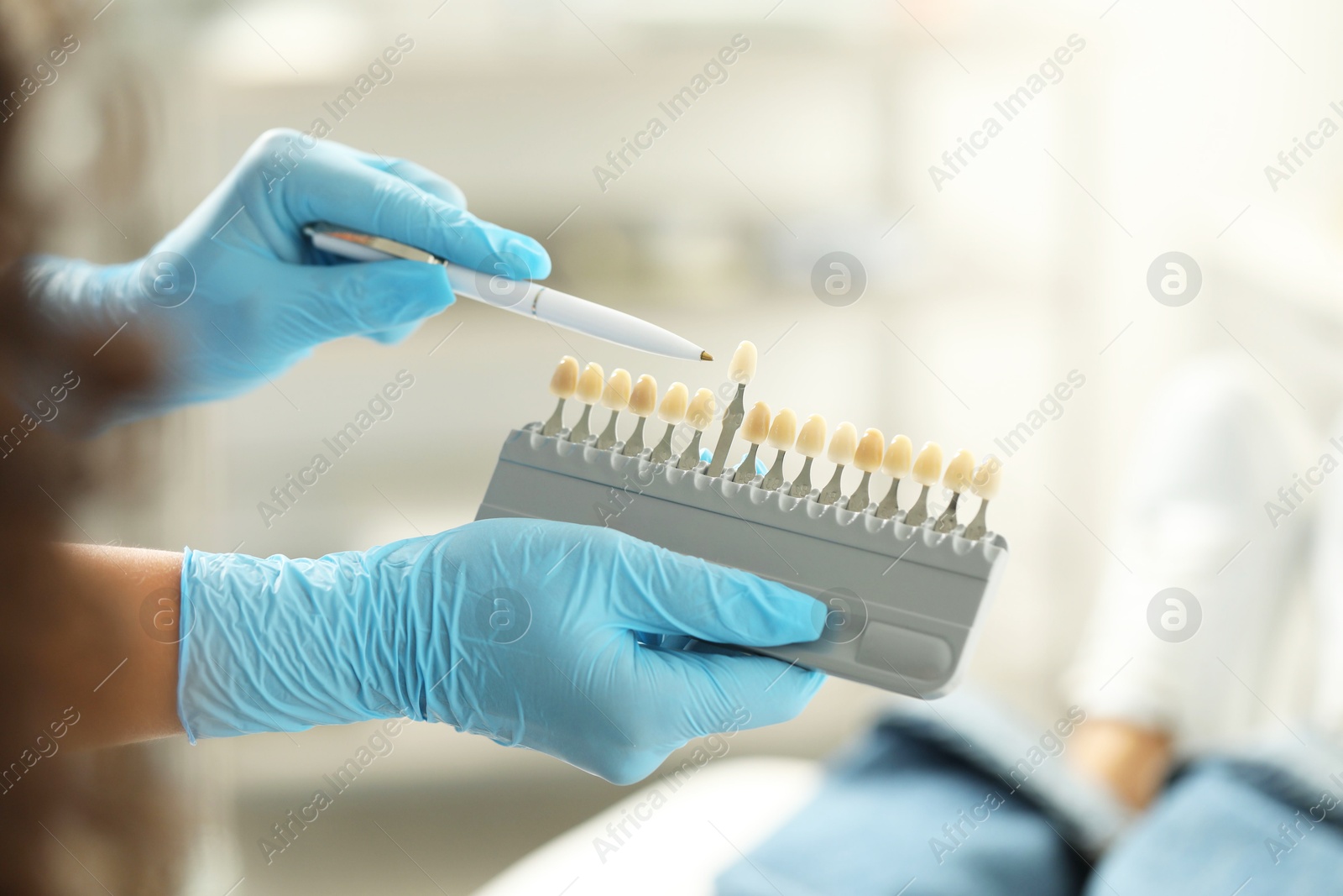 Photo of Doctor and patient choosing shade on teeth color palette in clinic, closeup. Dental veneers