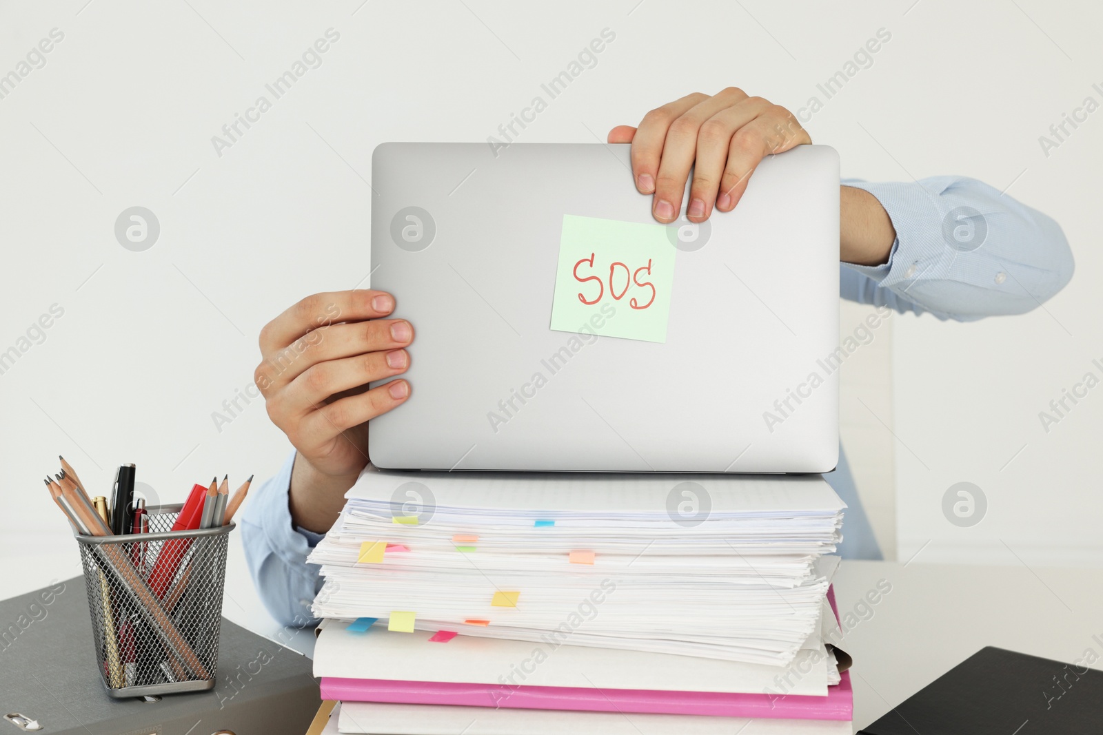 Photo of Man hiding face behind laptop with word SOS at table on light background