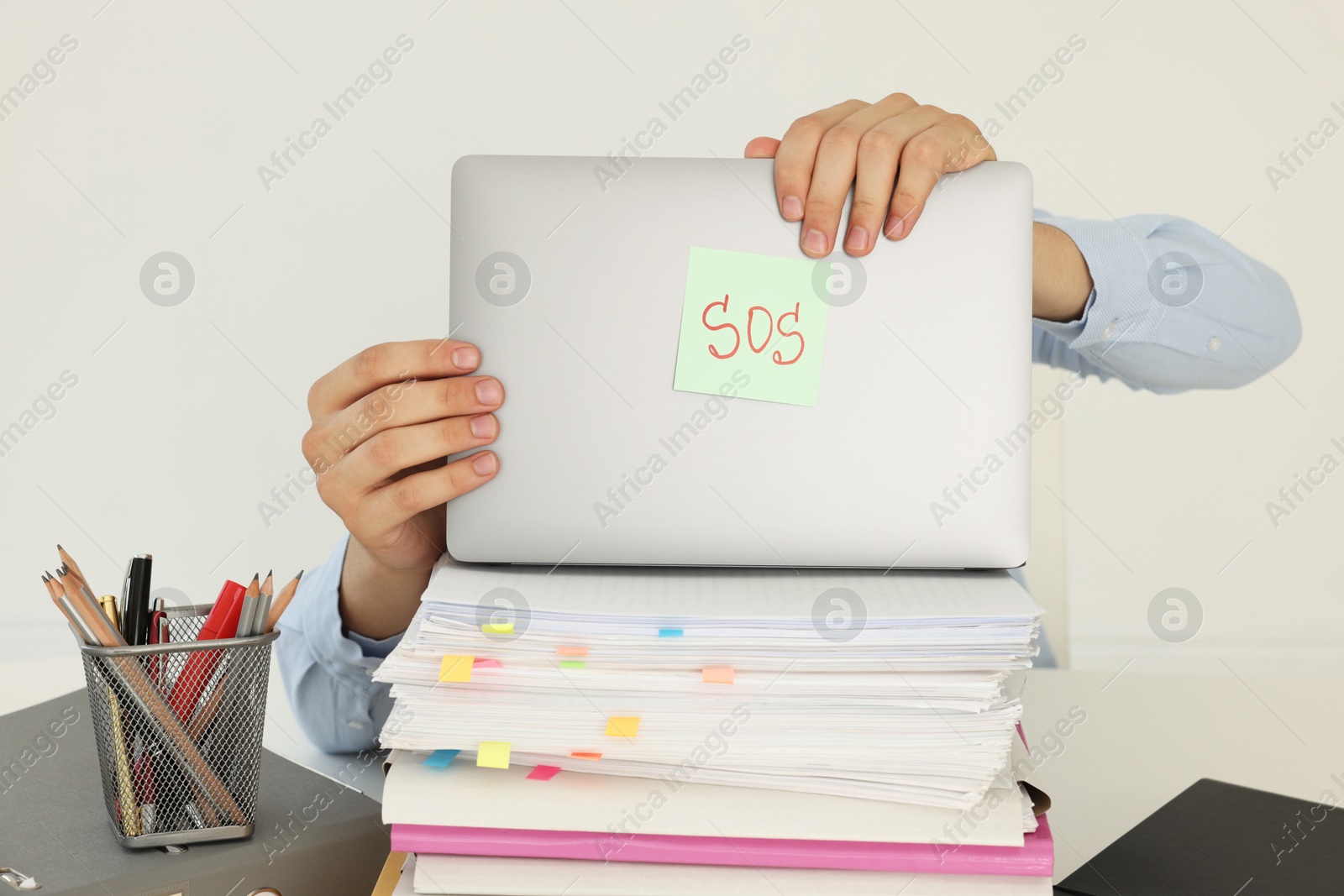 Photo of Man hiding face behind laptop with word SOS at table on light background