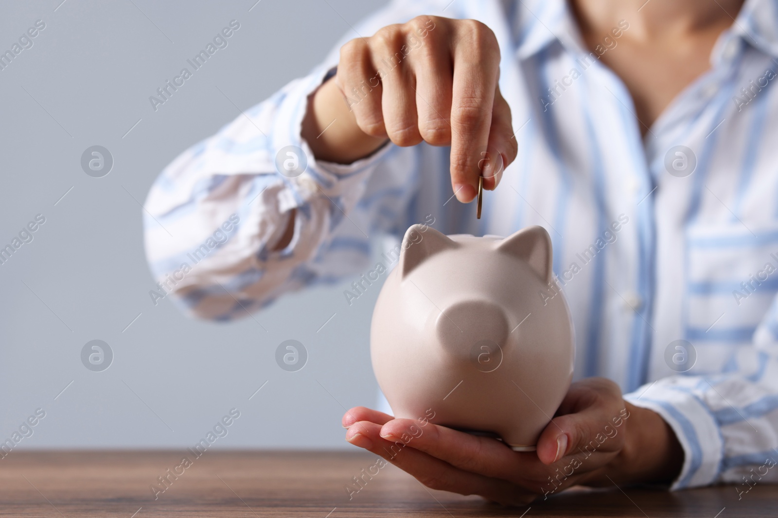 Photo of Woman putting coin into piggy bank at wooden table, closeup