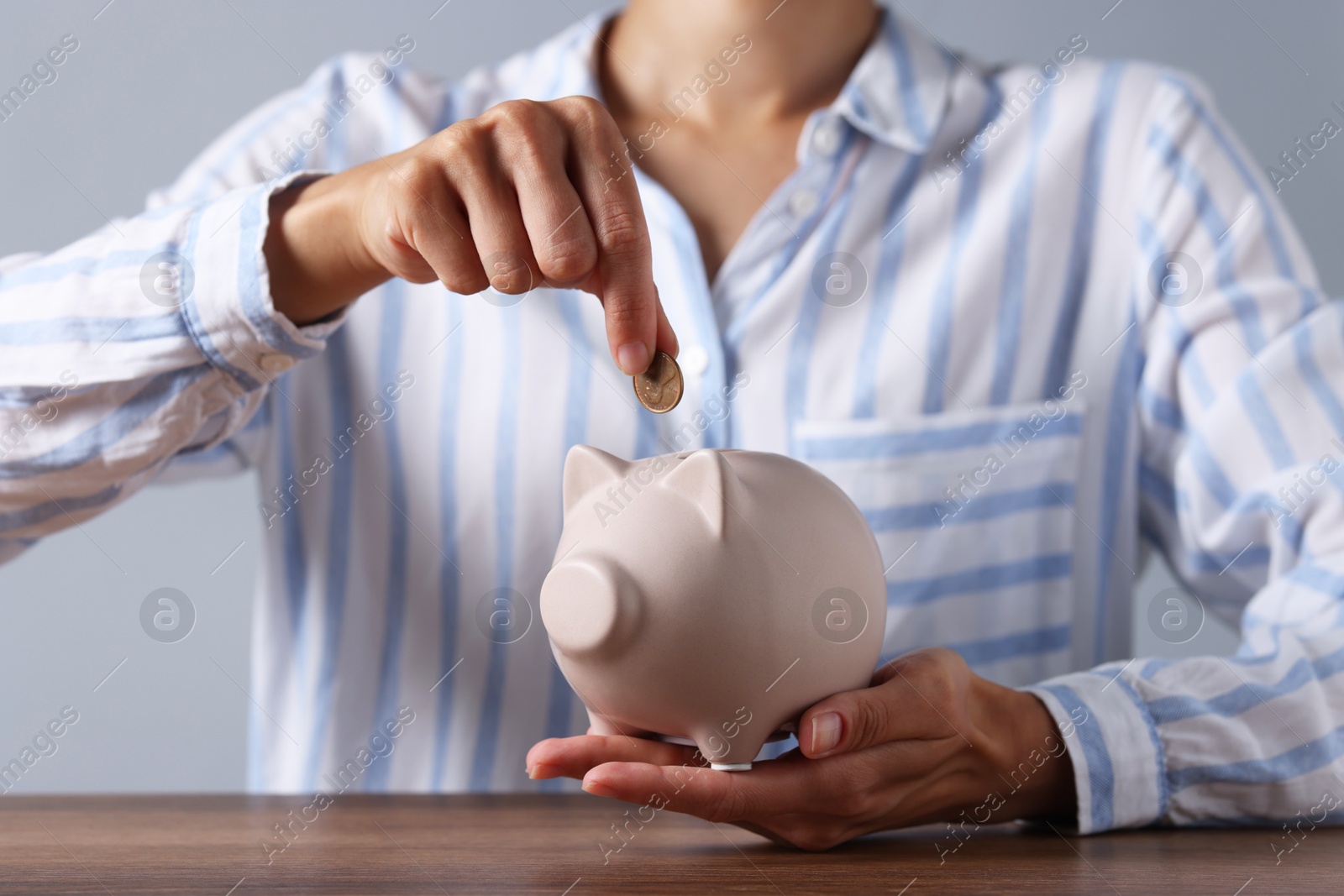 Photo of Woman putting coin into piggy bank at wooden table, closeup