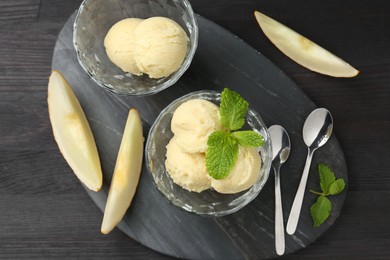 Scoops of melon sorbet with mint in glass dessert bowls, fresh fruit and spoons on dark wooden table, flat lay