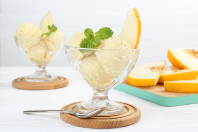 Photo of Scoops of melon sorbet with mint in glass dessert bowls and spoon on white wooden table, closeup