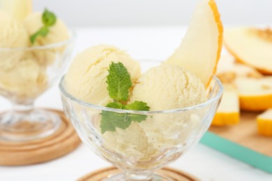 Photo of Scoops of melon sorbet with mint and fresh fruit in glass dessert bowls on white table, closeup