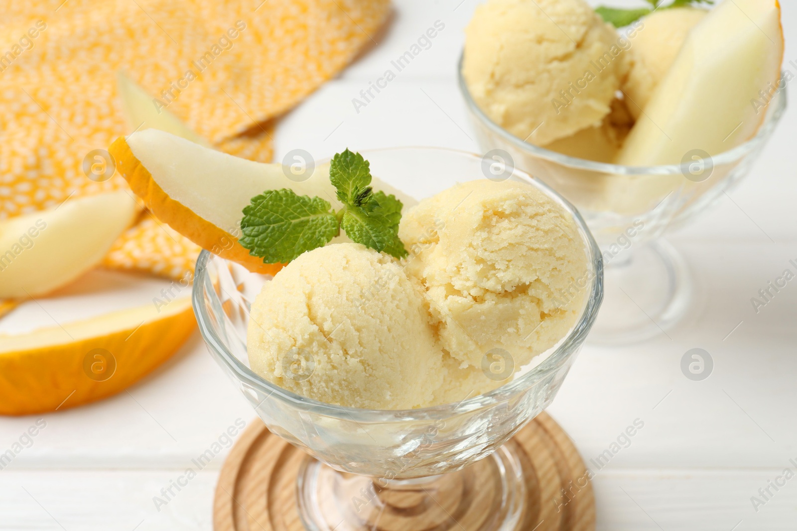 Photo of Scoops of melon sorbet with mint and fresh fruit in glass dessert bowls on white wooden table, closeup