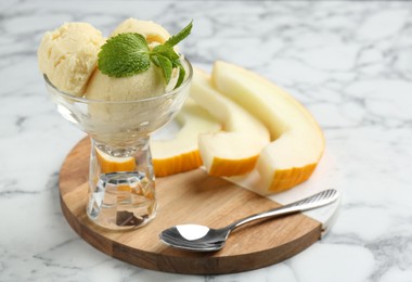 Photo of Scoops of melon sorbet with mint in glass dessert bowl, fresh fruit and spoon on light marble table, closeup