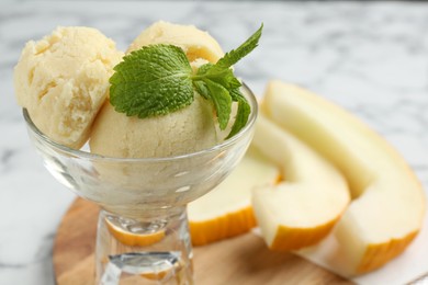 Photo of Scoops of melon sorbet with mint in glass dessert bowl and fresh fruit on light table, closeup