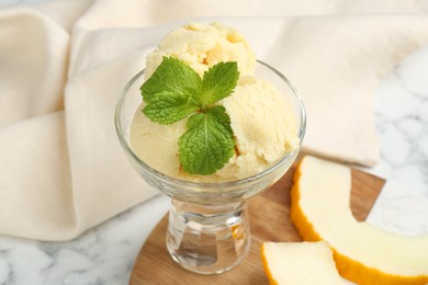 Photo of Scoops of melon sorbet with mint in glass dessert bowl and fresh fruit on light table, closeup