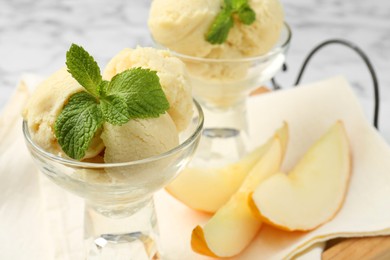 Photo of Scoops of melon sorbet with mint in glass dessert bowls and fresh fruit on light table, closeup