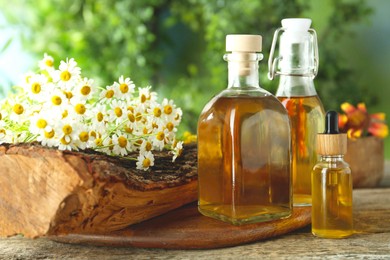 Photo of Different tinctures in bottles and chamomile flowers on wooden table