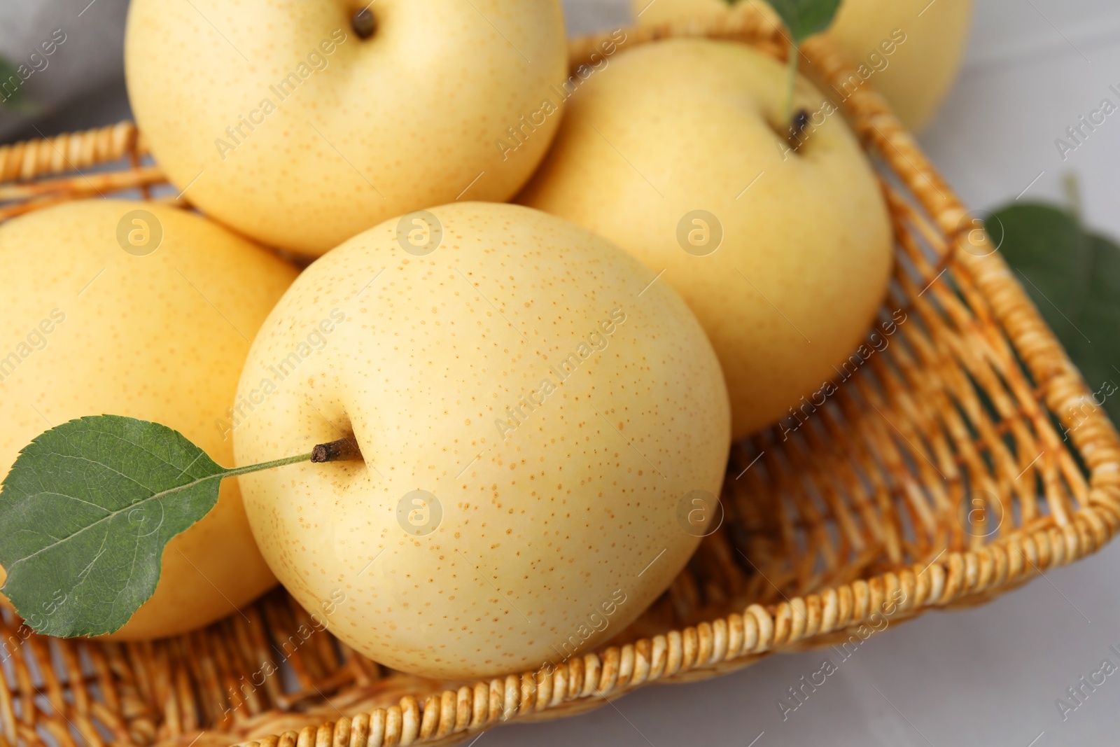 Photo of Delicious fresh apple pears in wicker basket and green leaf on table, closeup