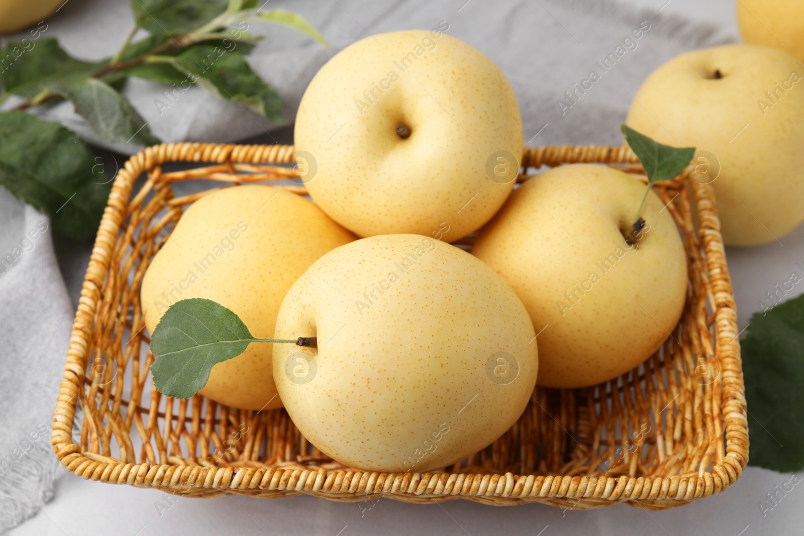 Photo of Delicious fresh apple pears in wicker basket and green leaves on table, closeup