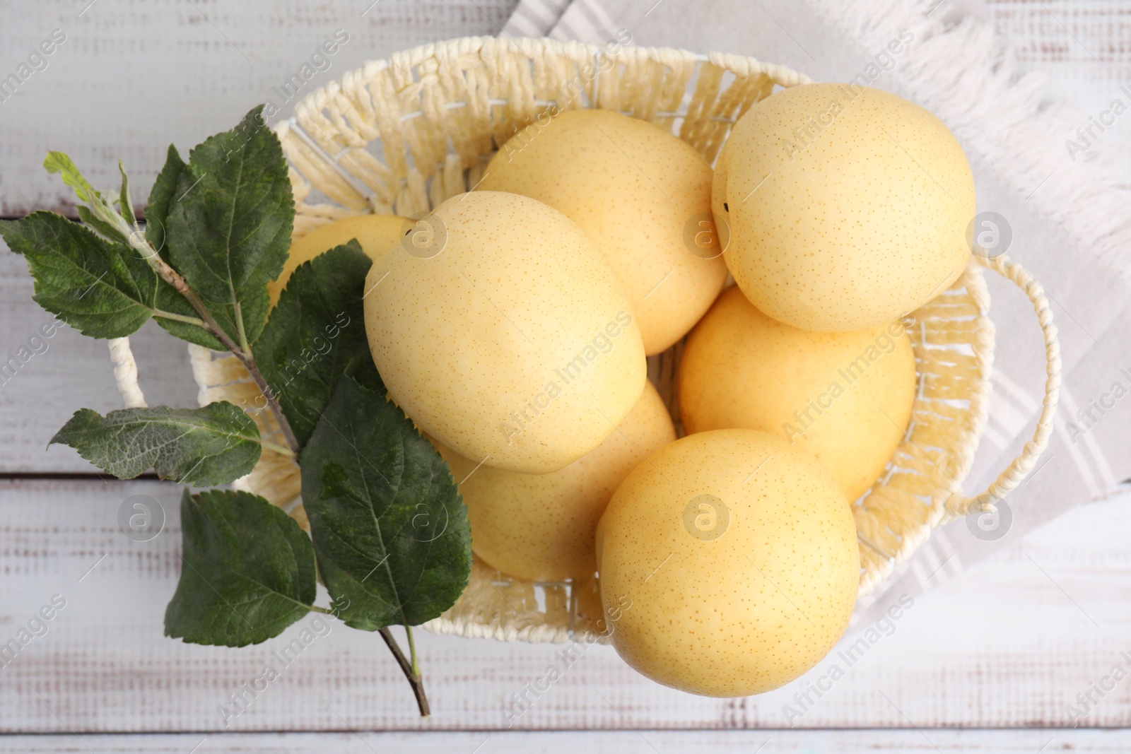 Photo of Delicious fresh apple pears in wicker basket and green leaves on white wooden table, top view