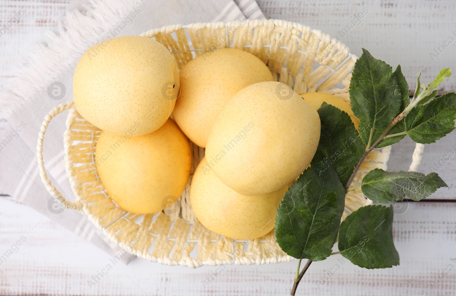 Photo of Delicious fresh apple pears in wicker basket and green leaves on white wooden table, top view