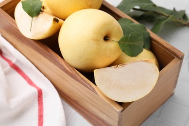 Photo of Delicious fresh apple pears in wooden crate and green leaves on white table, closeup