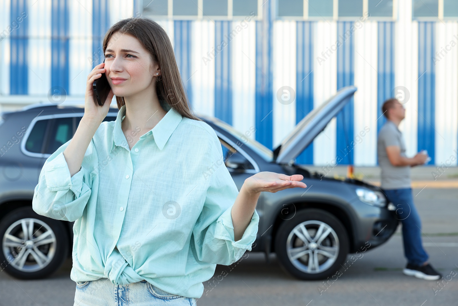 Photo of Man standing near broken auto while woman calling to car service outdoors