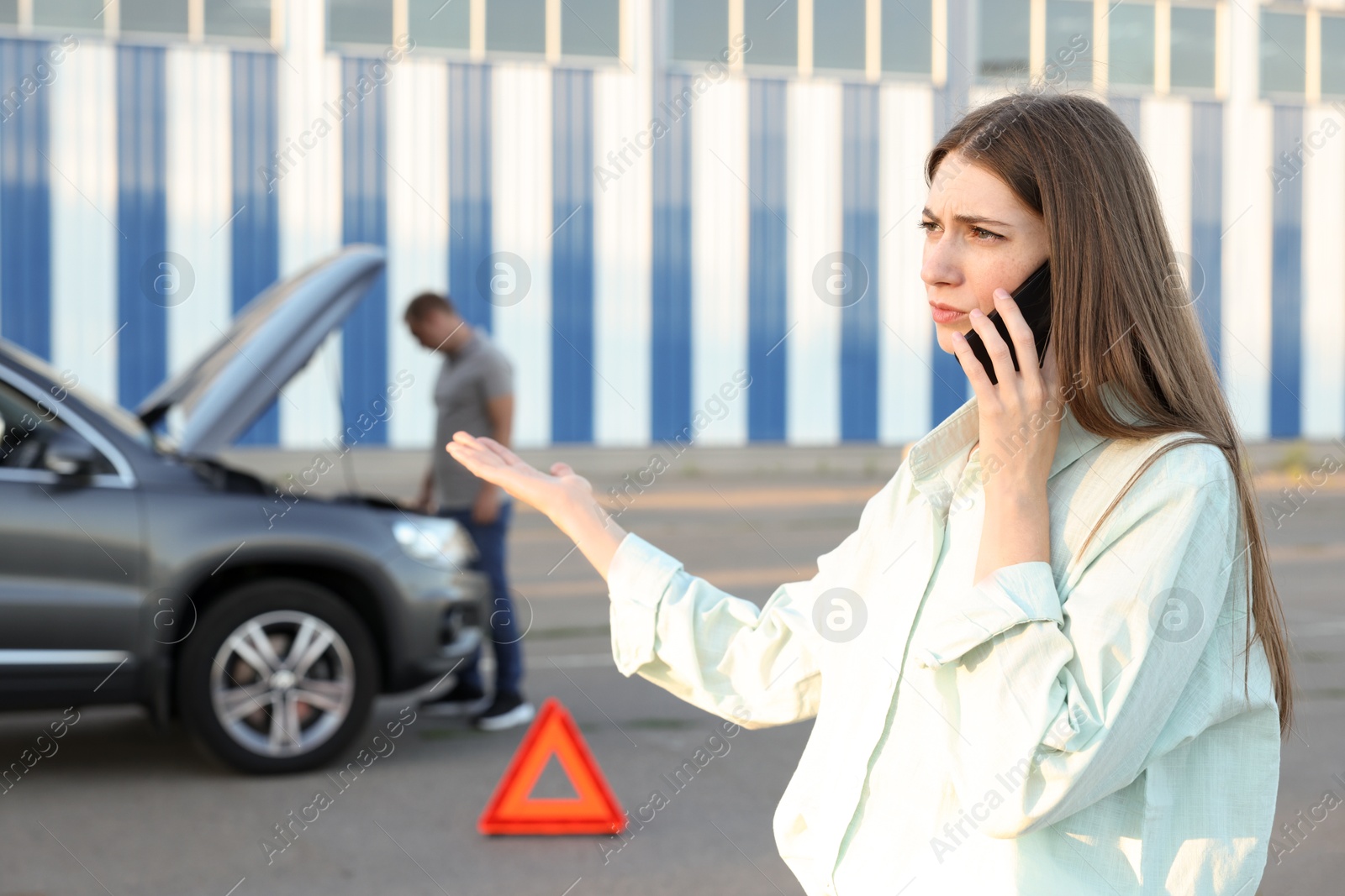 Photo of Man standing near broken auto while woman calling to car service outdoors