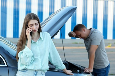 Photo of Man examining broken auto while woman calling to car service outdoors