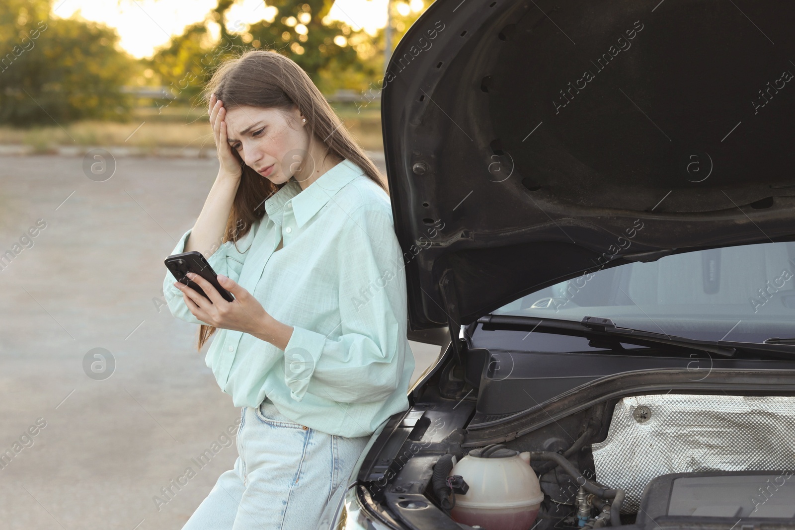 Photo of Stressed woman using smartphone near broken car outdoors