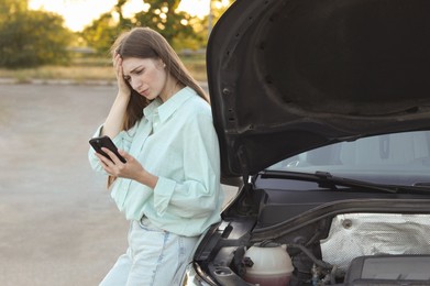 Stressed woman using smartphone near broken car outdoors