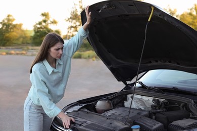 Photo of Stressed woman looking under hood of broken car outdoors