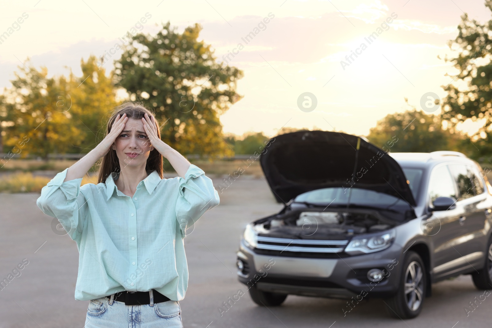 Photo of Stressed woman standing near broken car outdoors