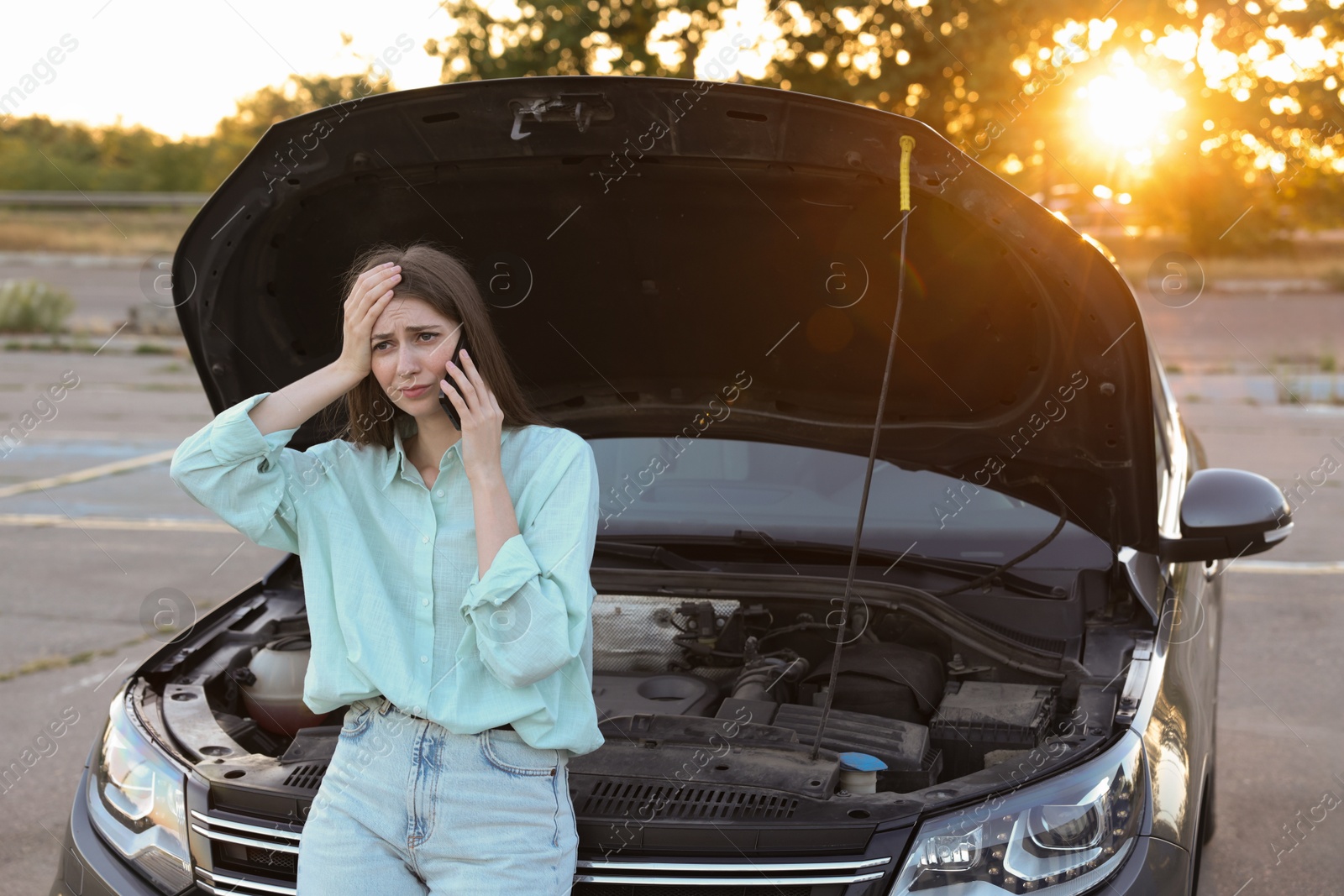 Photo of Stressed woman talking on phone near broken car outdoors