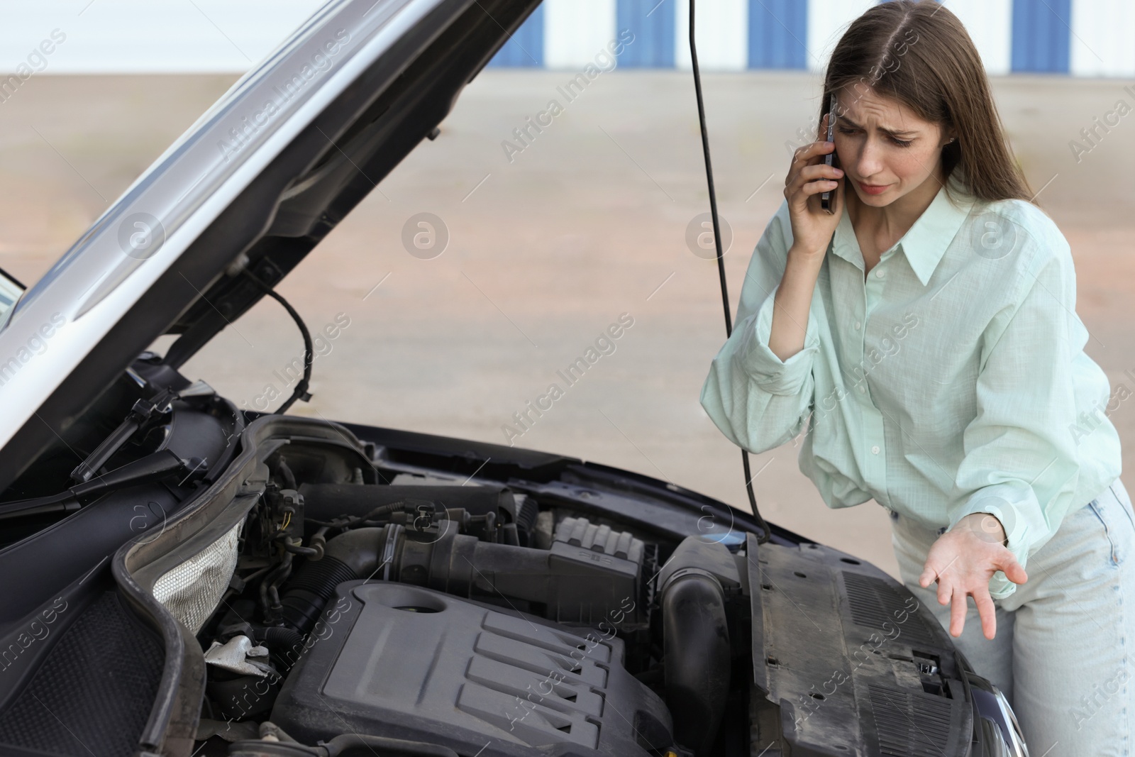 Photo of Stressed woman talking on phone near broken car outdoors