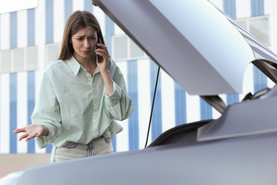 Photo of Stressed woman talking on phone near broken car outdoors