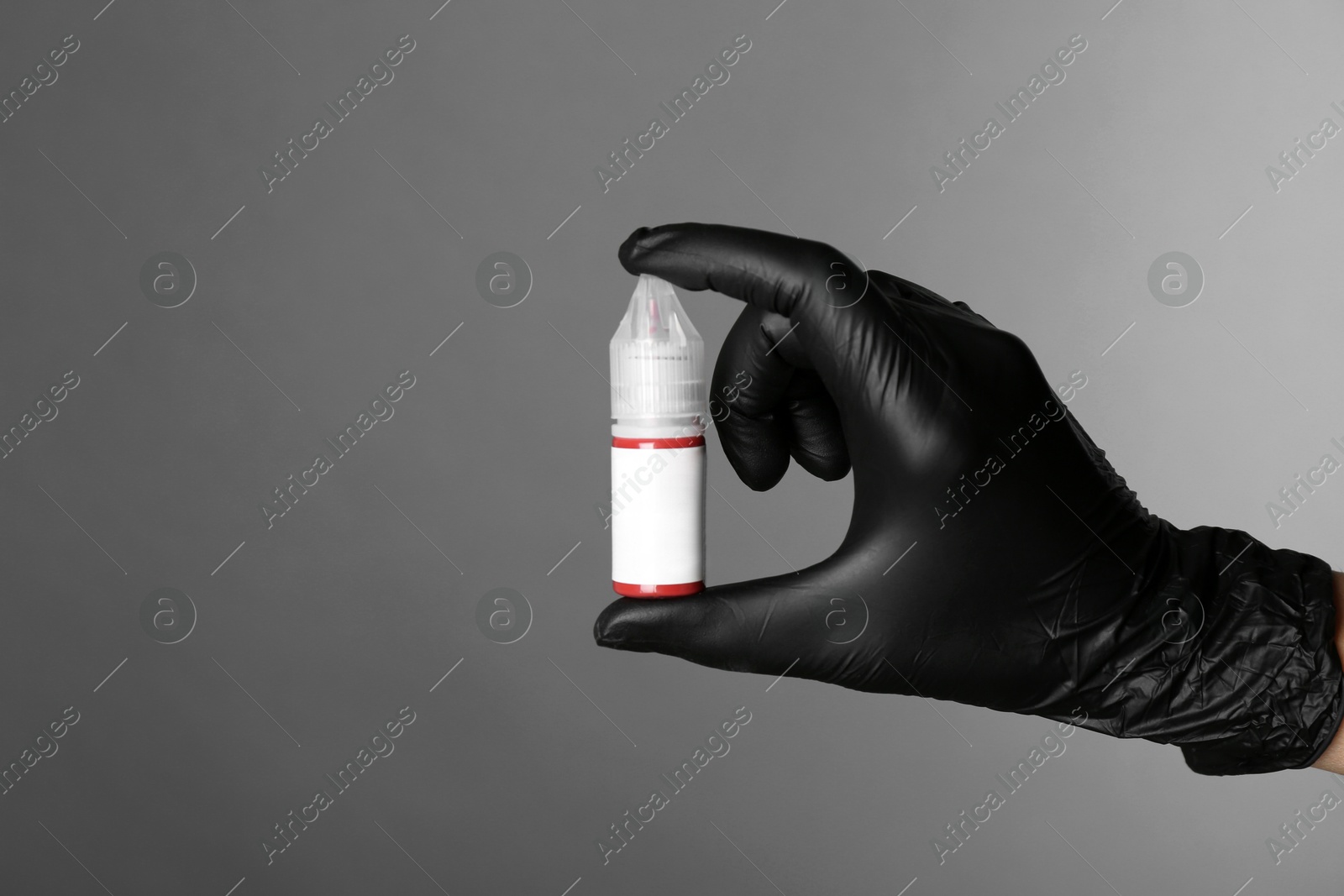 Photo of Professional cosmetologist holding bottle of pigment for permanent makeup on grey background, closeup. Space for text