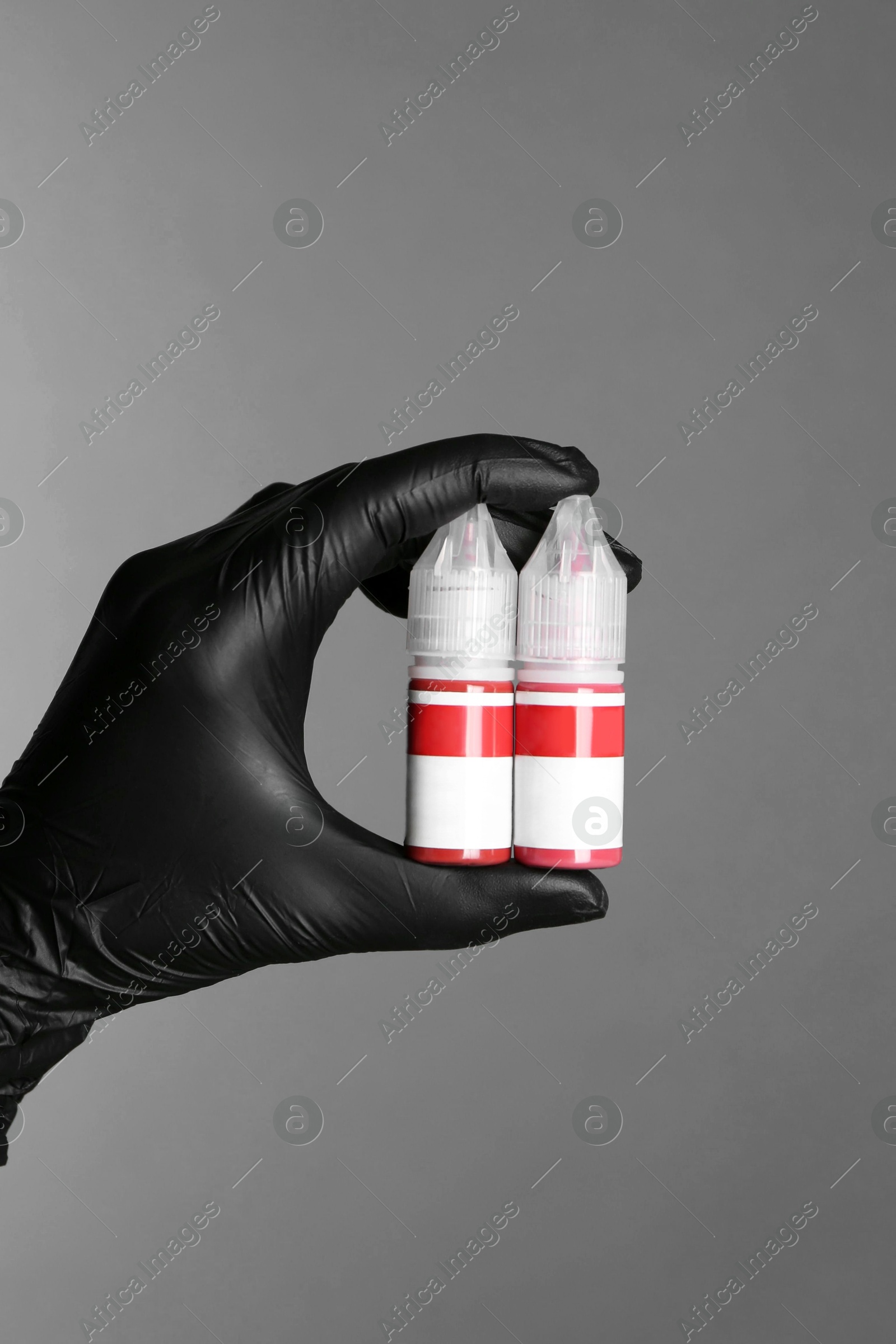 Photo of Professional cosmetologist holding bottles of pigments for permanent makeup on grey background, closeup