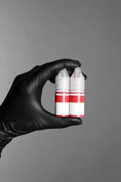 Professional cosmetologist holding bottles of pigments for permanent makeup on grey background, closeup