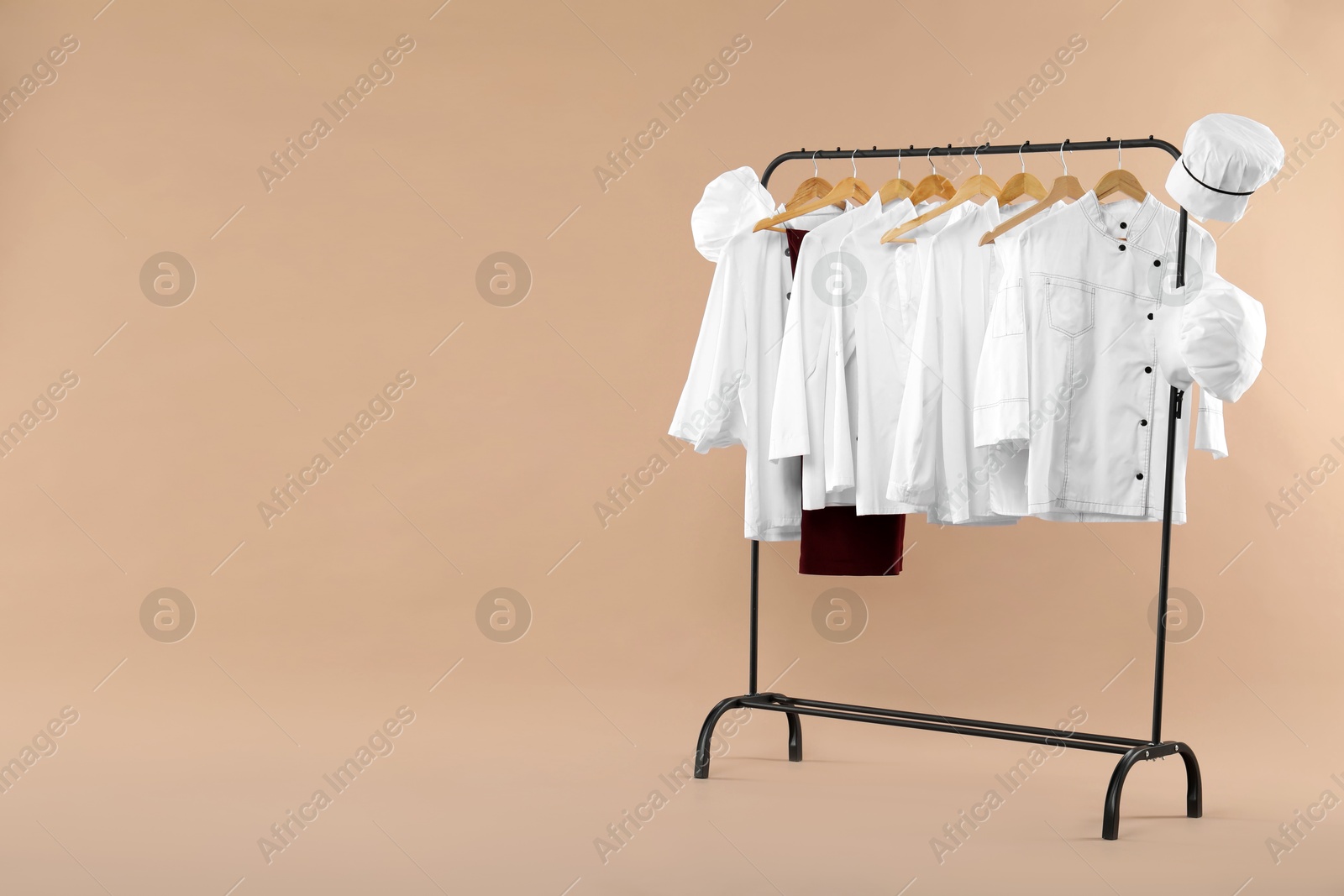 Photo of Different chef's uniforms on clothing rack against beige background, space for text