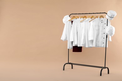 Photo of Different chef's uniforms on clothing rack against beige background, space for text