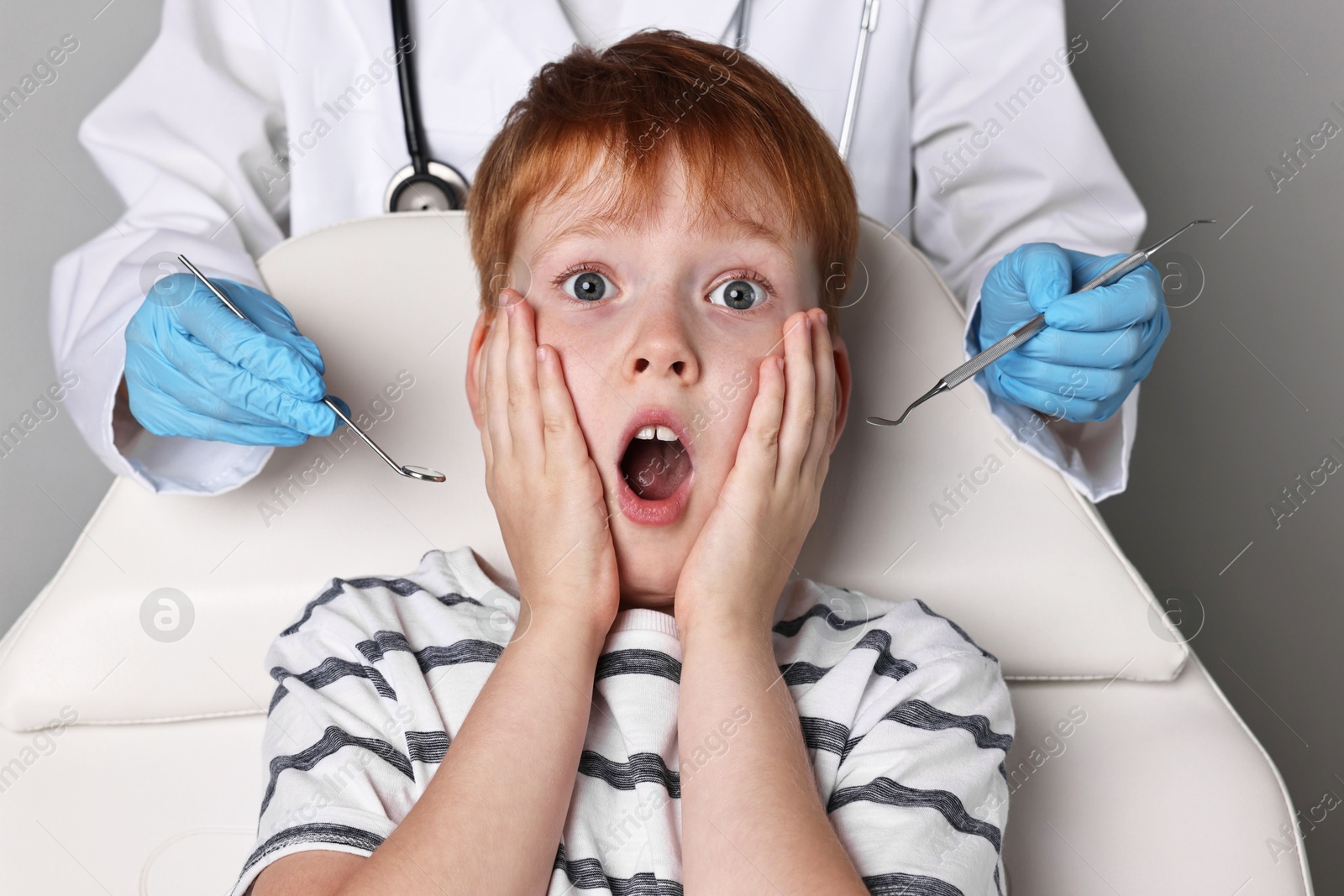 Photo of Dental phobia. Dentist working with scared little boy on grey background