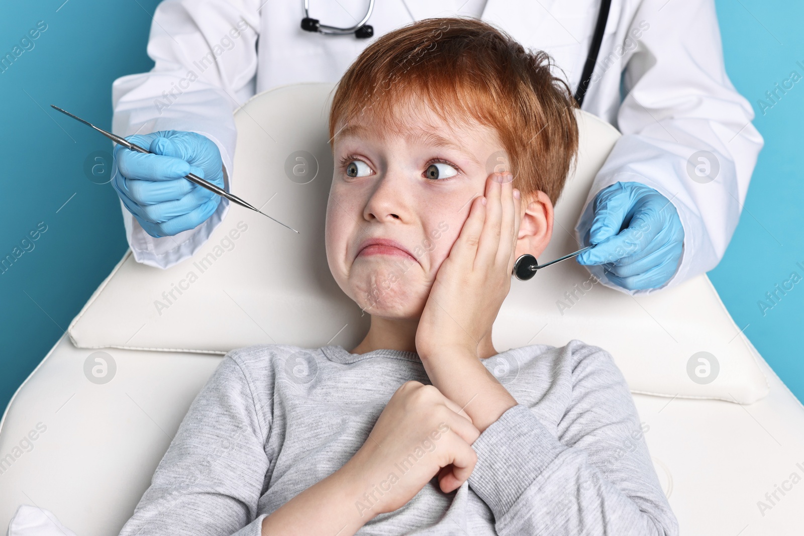 Photo of Dental phobia. Dentist working with scared little boy on light blue background