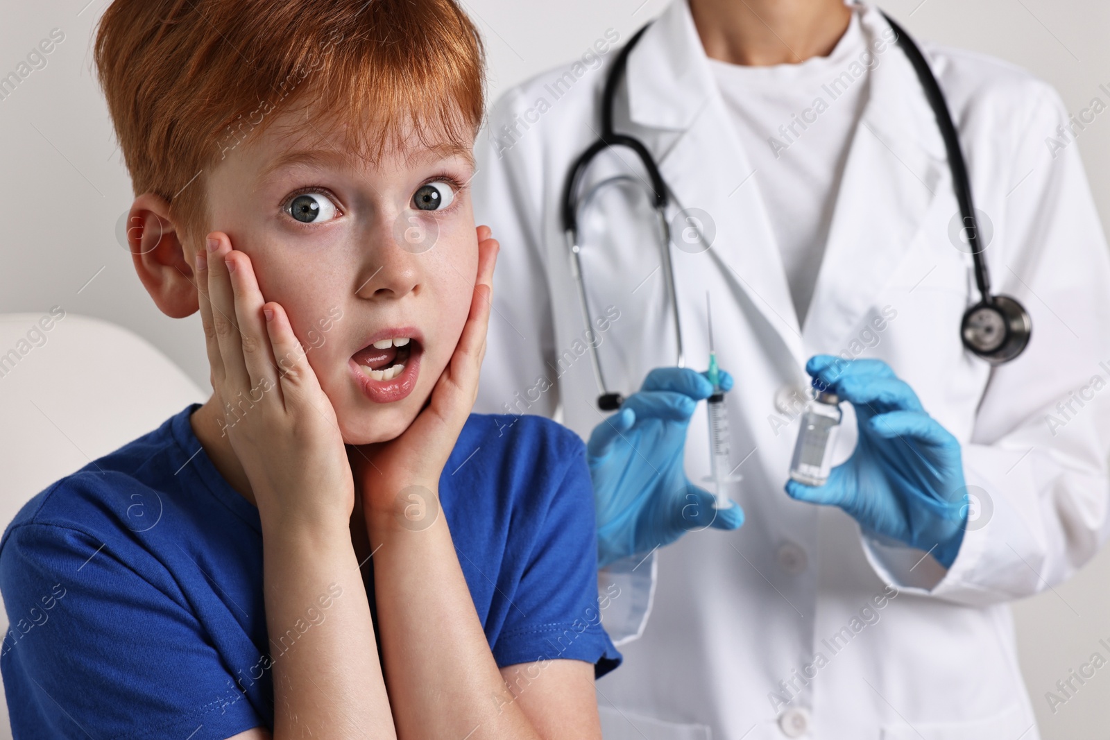 Photo of Dental phobia. Scared boy near dentist with syringe and vial on light grey background