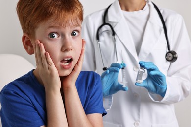 Dental phobia. Scared boy near dentist with syringe and vial on light grey background