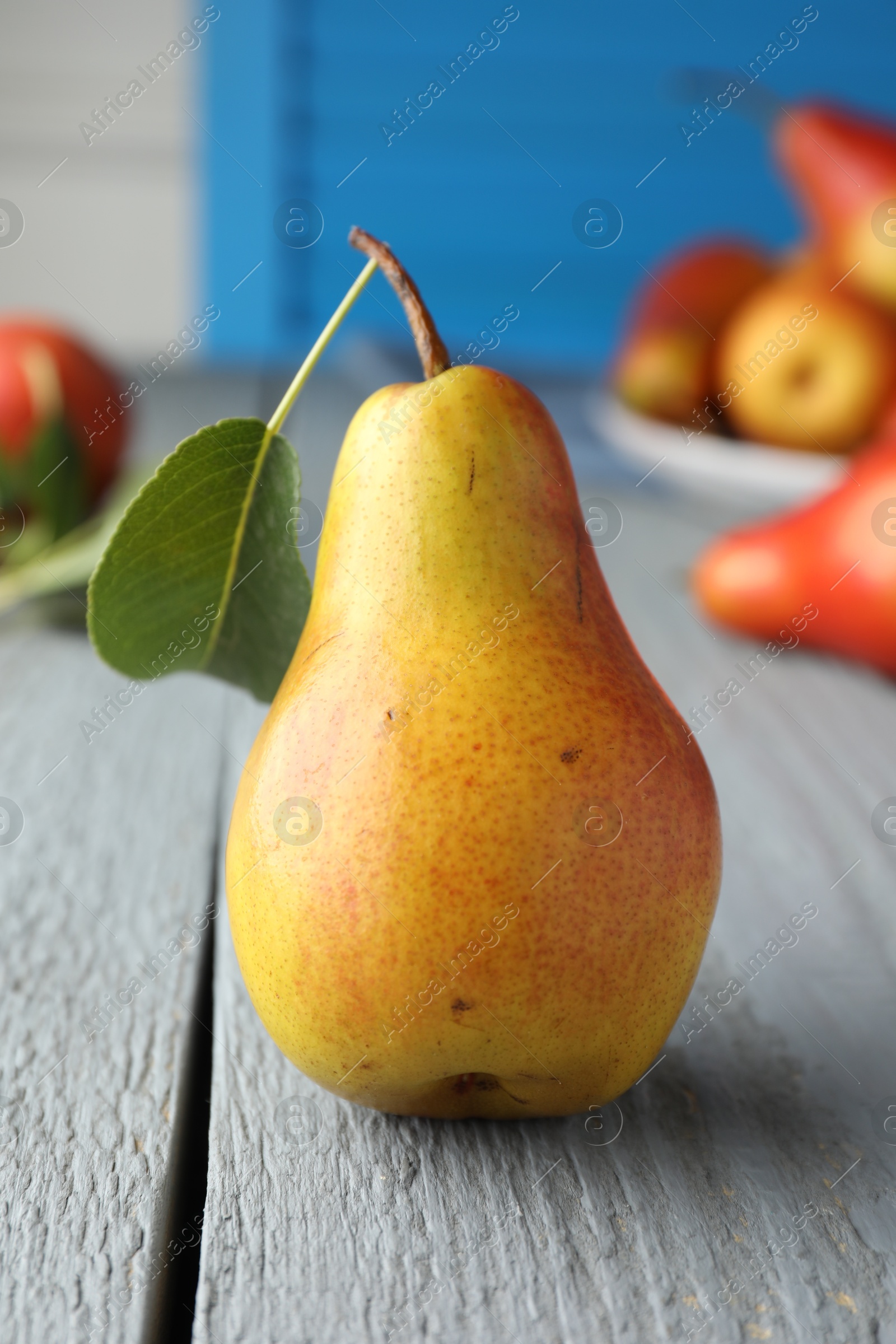 Photo of Ripe juicy pear with green leaf on grey wooden table