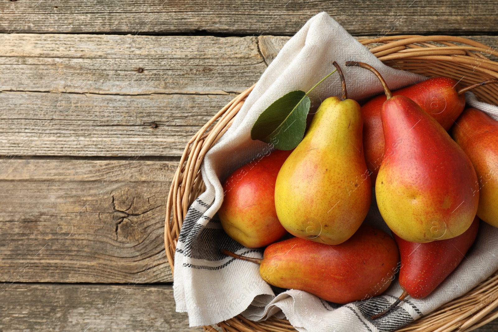 Photo of Ripe juicy pears in wicker basket on wooden table, top view. Space for text