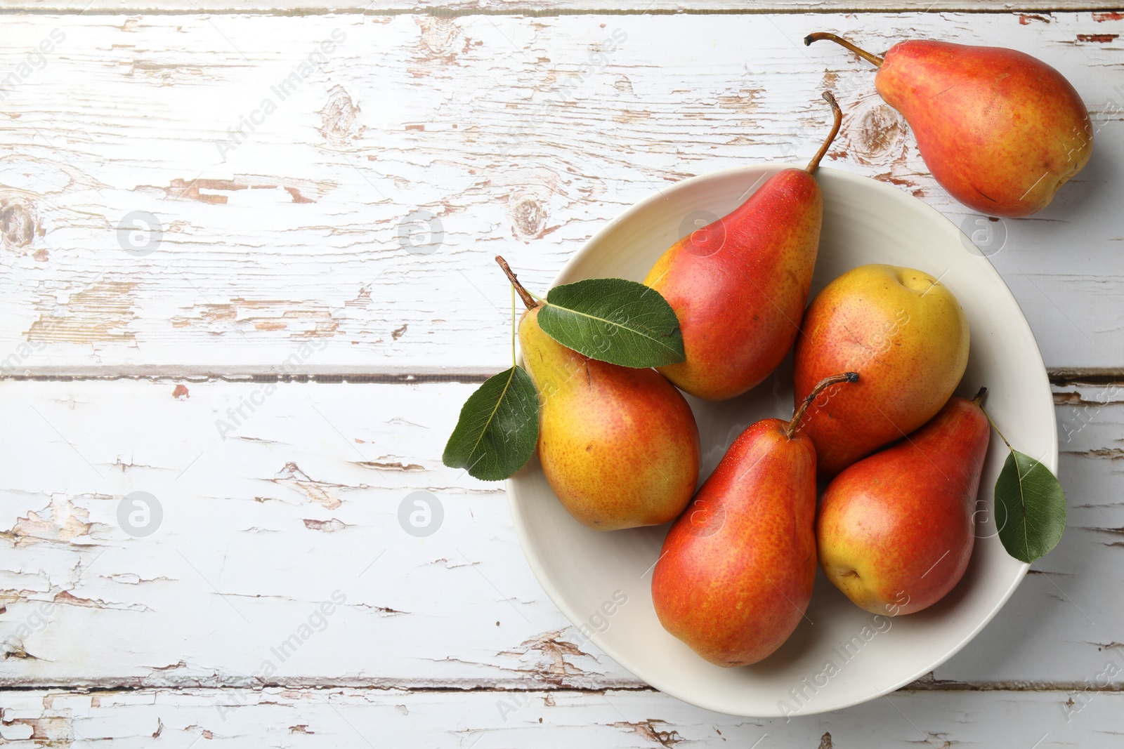 Photo of Ripe juicy pears in bowl on light wooden table, top view. Space for text