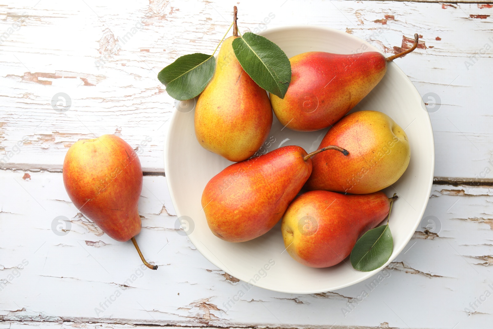 Photo of Ripe juicy pears in bowl on light wooden table, top view