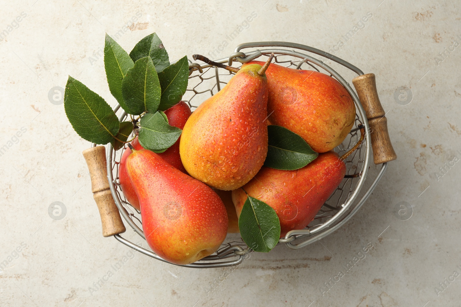 Photo of Ripe juicy pears in metal basket on grey textured table, top view