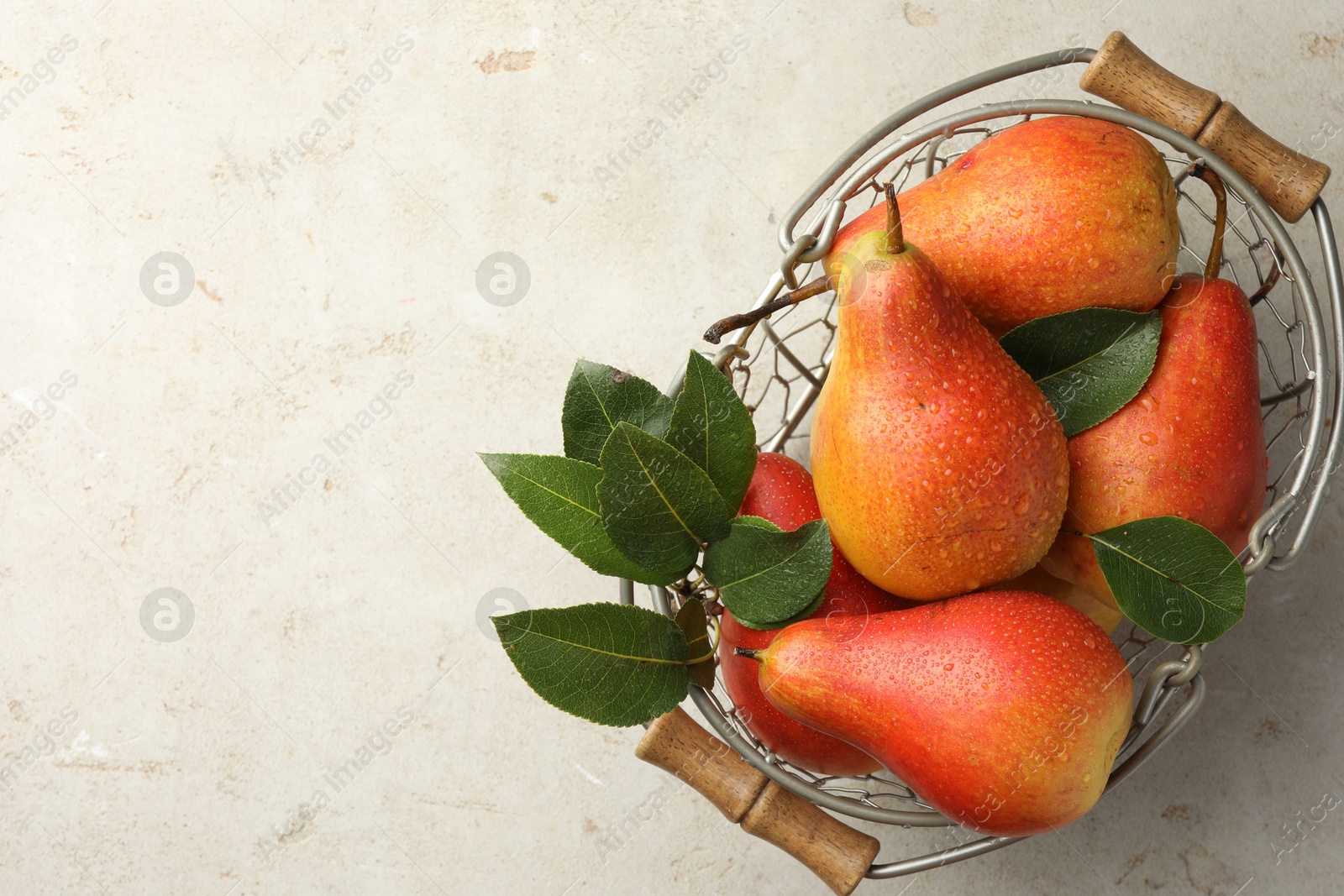 Photo of Ripe juicy pears in metal basket on grey textured table, top view. Space for text