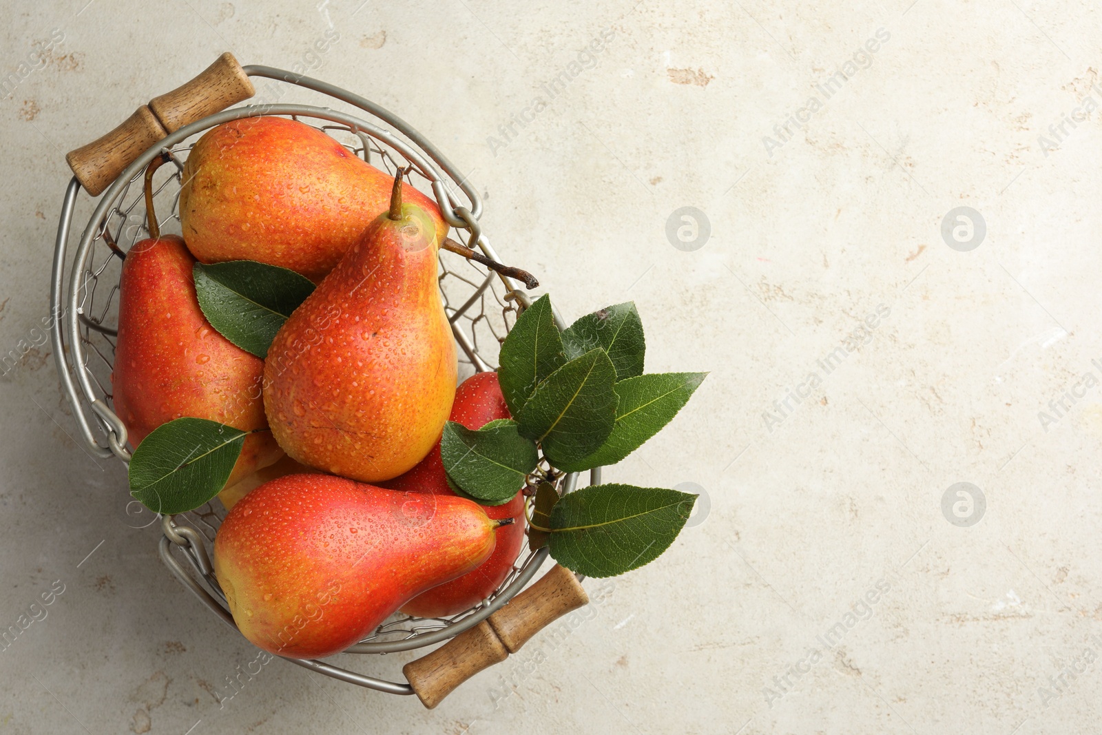 Photo of Ripe juicy pears in metal basket on grey textured table, top view. Space for text