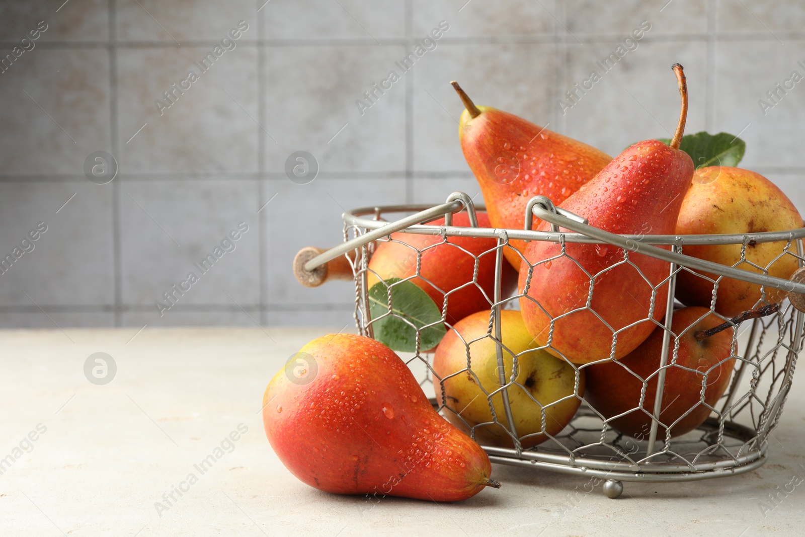 Photo of Ripe juicy pears in metal basket on grey textured table, space for text