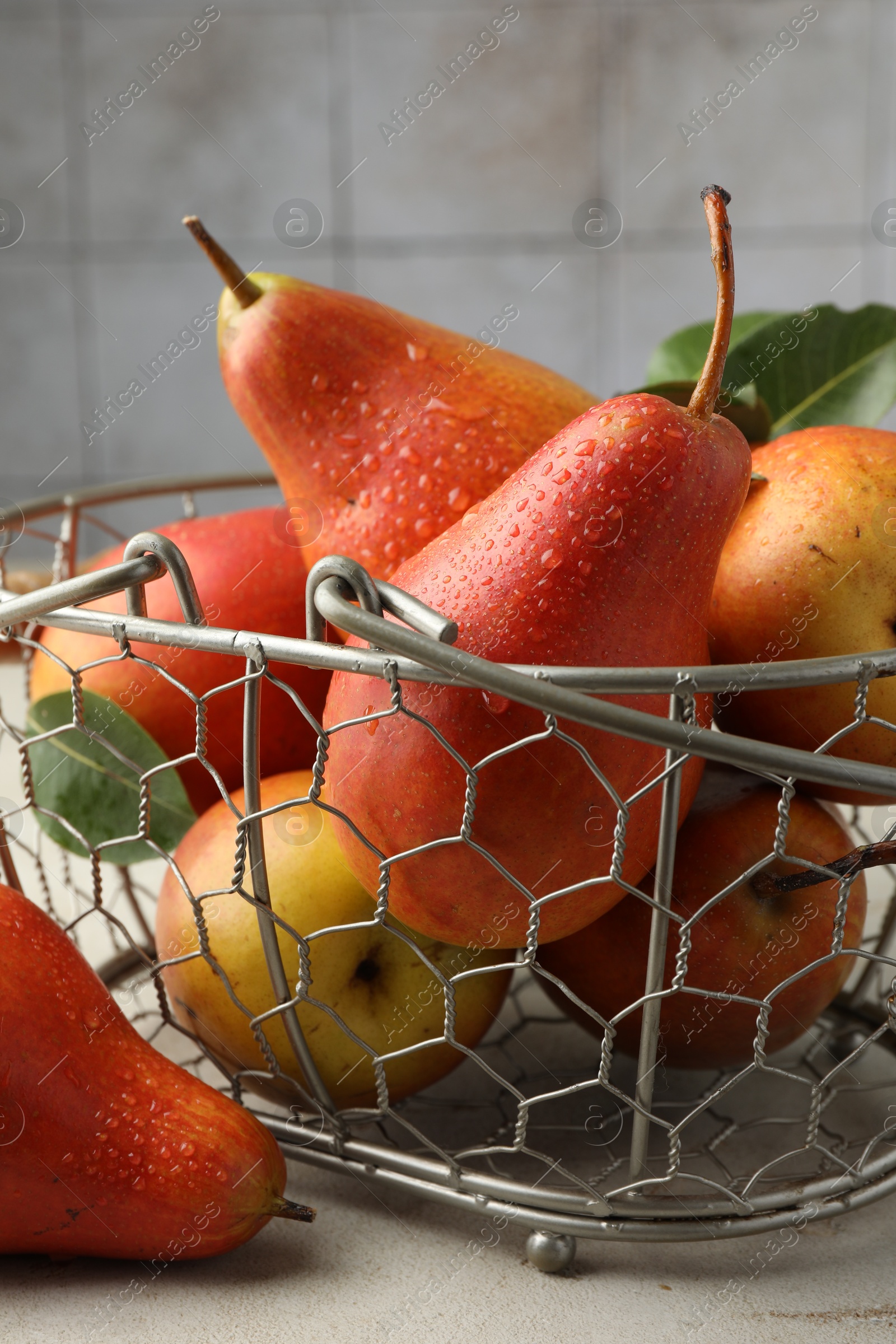 Photo of Ripe juicy pears in metal basket on grey textured table, closeup