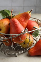 Photo of Ripe juicy pears in metal basket on grey textured table, closeup