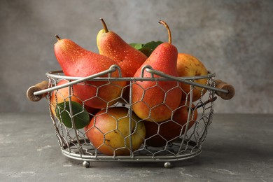 Photo of Ripe juicy pears in metal basket on grey textured table