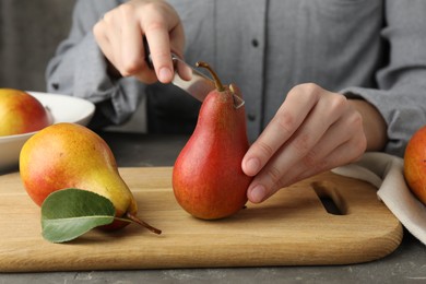 Photo of Woman cutting pear at grey textured table, closeup